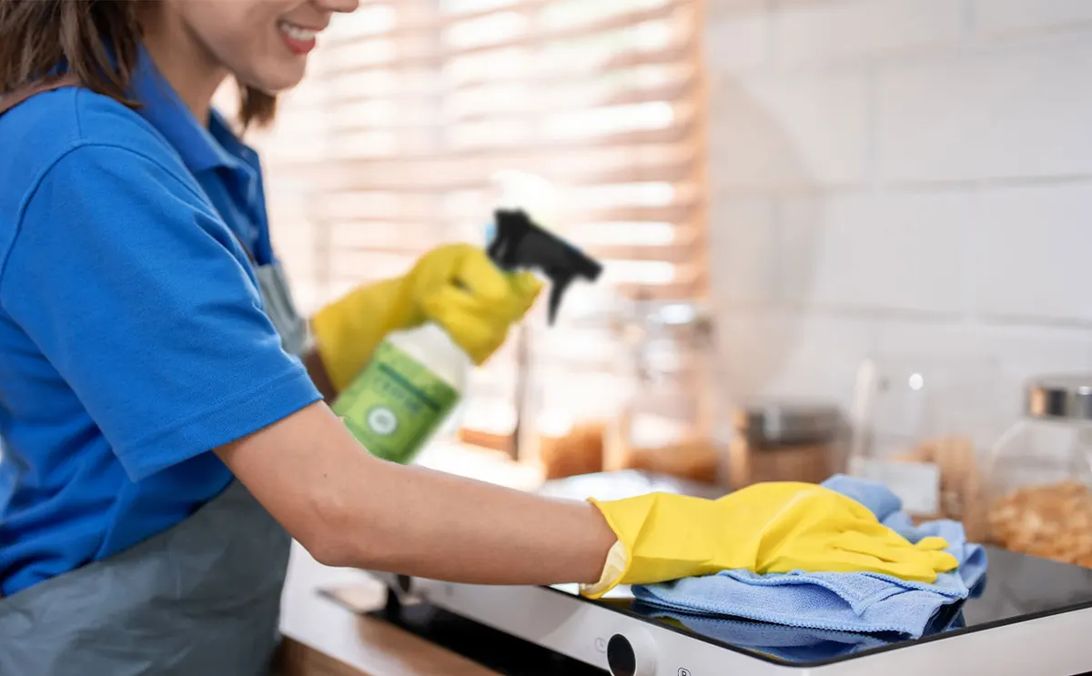 Persona con guantes limpiando la mesada de una cocina con un paño y un rociador