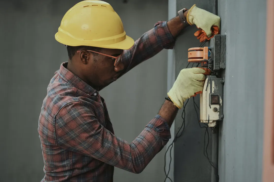 Electricista con casco y guantes revisando una instalación eléctrica en la pared