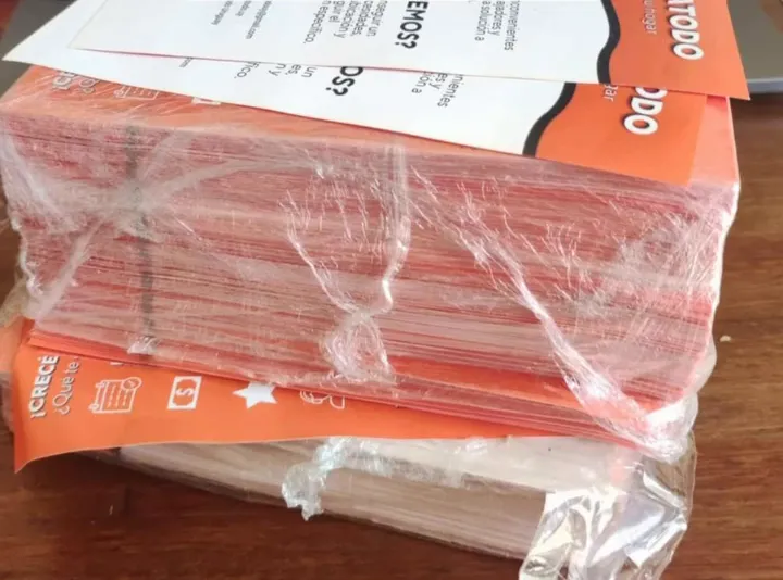 Pila de volantes naranjas de ArreglaTodo envueltos en nylon, listos para repartir