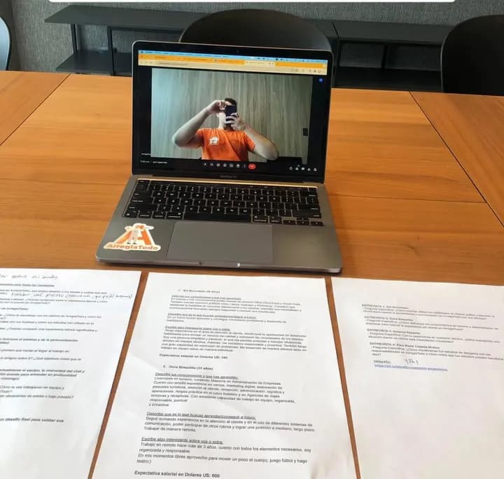 Videollamada en una notebook sobre una mesa de reuniones, con documentos impresos